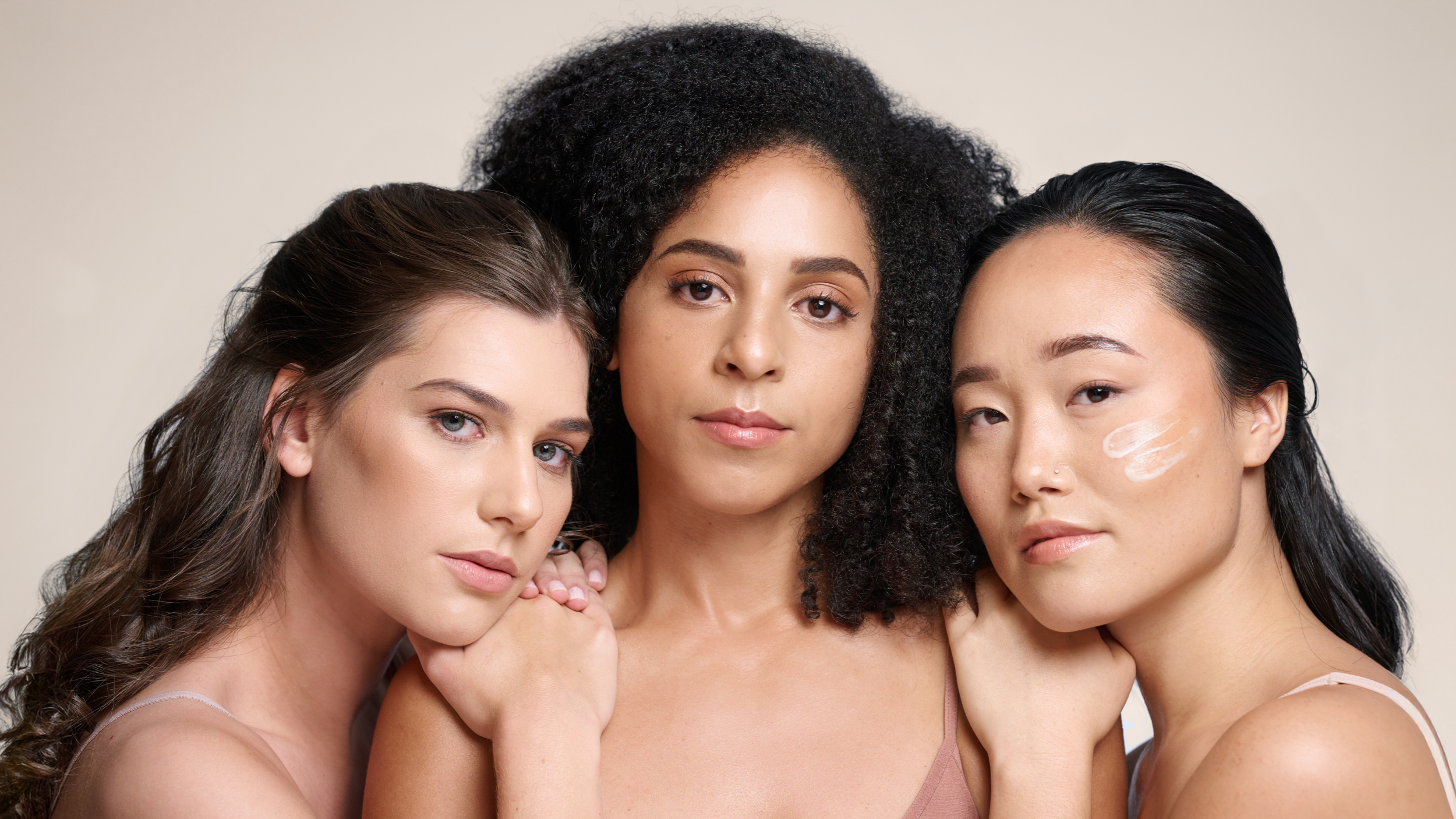 Three women with different hair and skin tones posing together against a neutral background